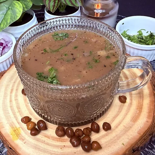 kala chana soup in a glass mug topped with chopped onion, black pepper and fresh coriander