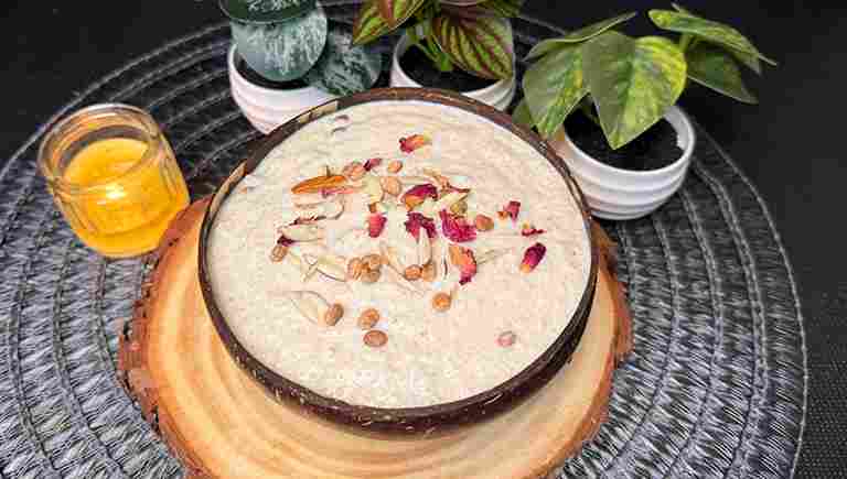 Creamy no-sugar samak kheer in a coconut shell bowl topped with sliced almonds, raisins and dried rose petals